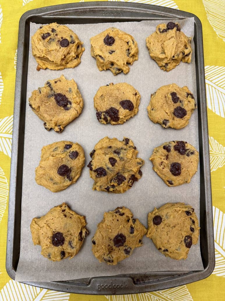 Pumpkin chocolate chip cookies freshly baked on a parchment-lined sheet pan, straight from the oven.