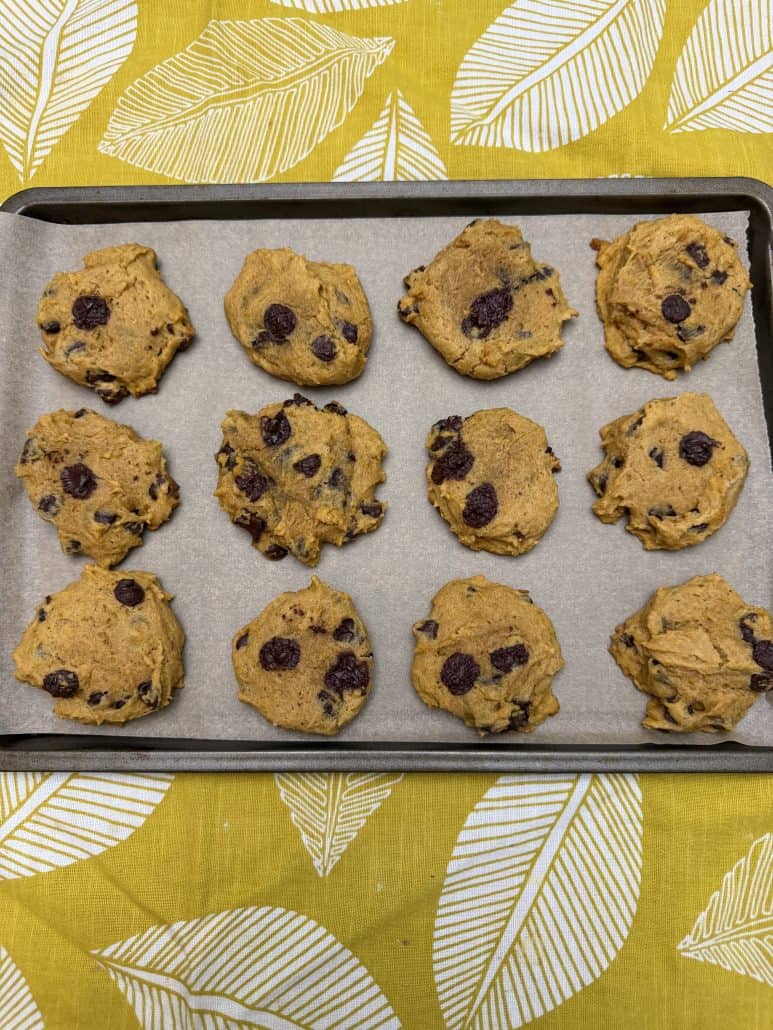 Pumpkin chocolate chip cookie dough scooped onto a parchment-lined baking sheet, ready to bake.