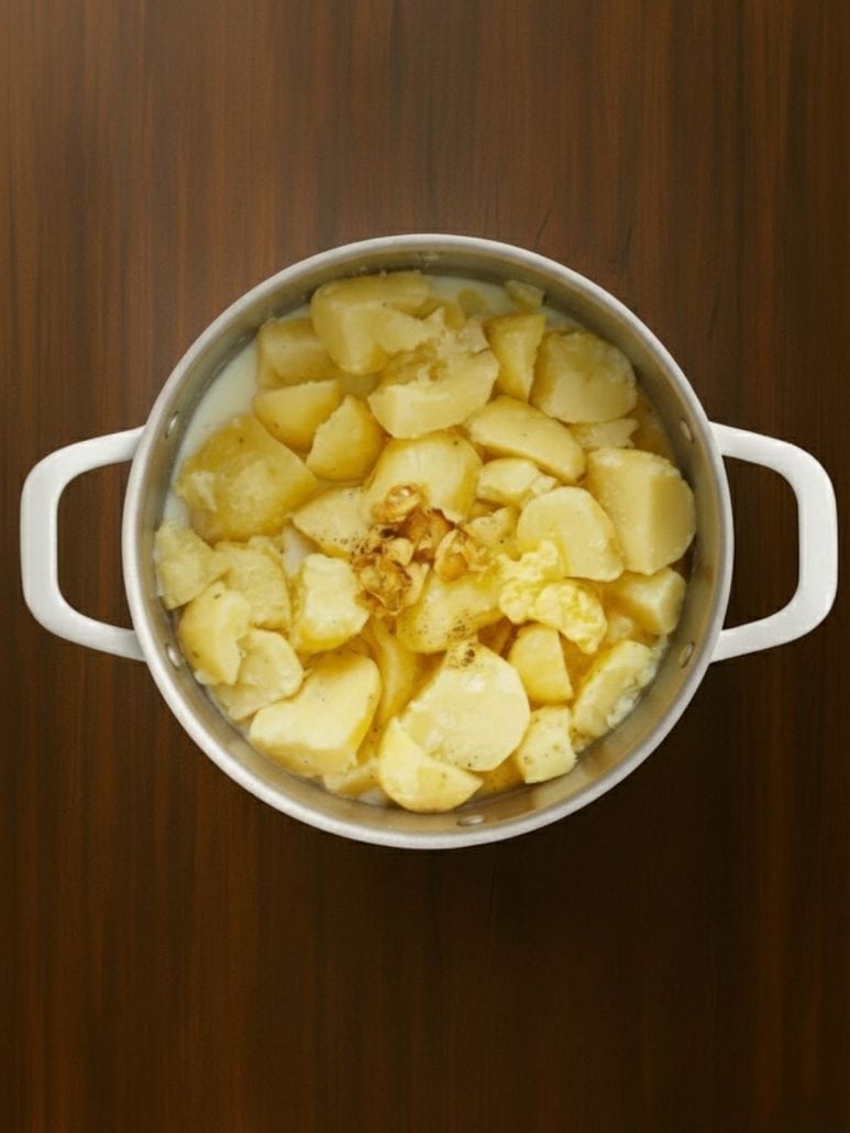 Cooked potatoes in a pot with milk, butter, and roasted garlicโready to be mashed.