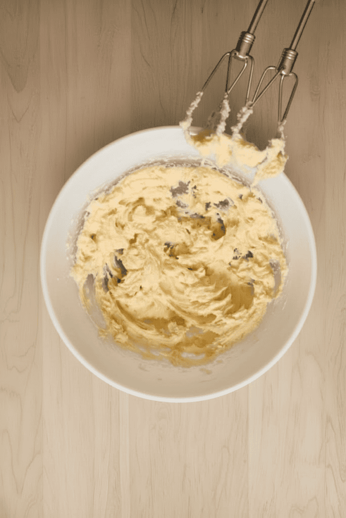 Creamed butter, powdered sugar, and vanilla in a mixing bowl with electric beaters—first step in preparing the dough for snowball cookies.
