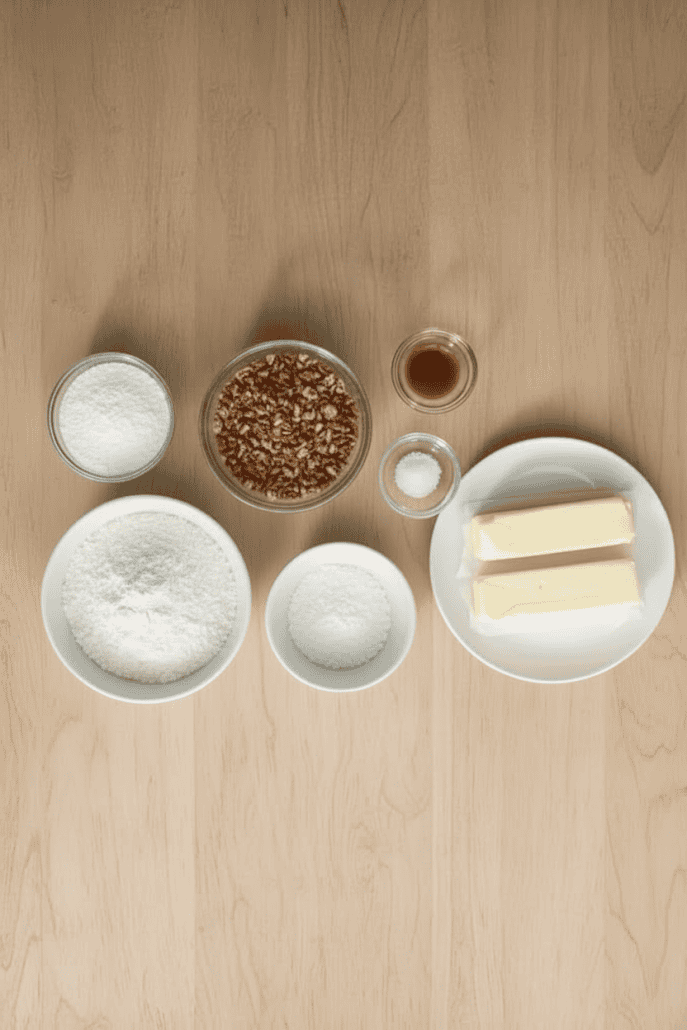 Overhead view of ingredients for snowball cookies, including butter, flour, powdered sugar, chopped pecans, vanilla, and salt.