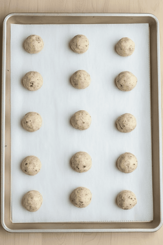 Unbaked snowball cookie dough balls arranged evenly on a parchment-lined baking sheet, ready to go into the oven.