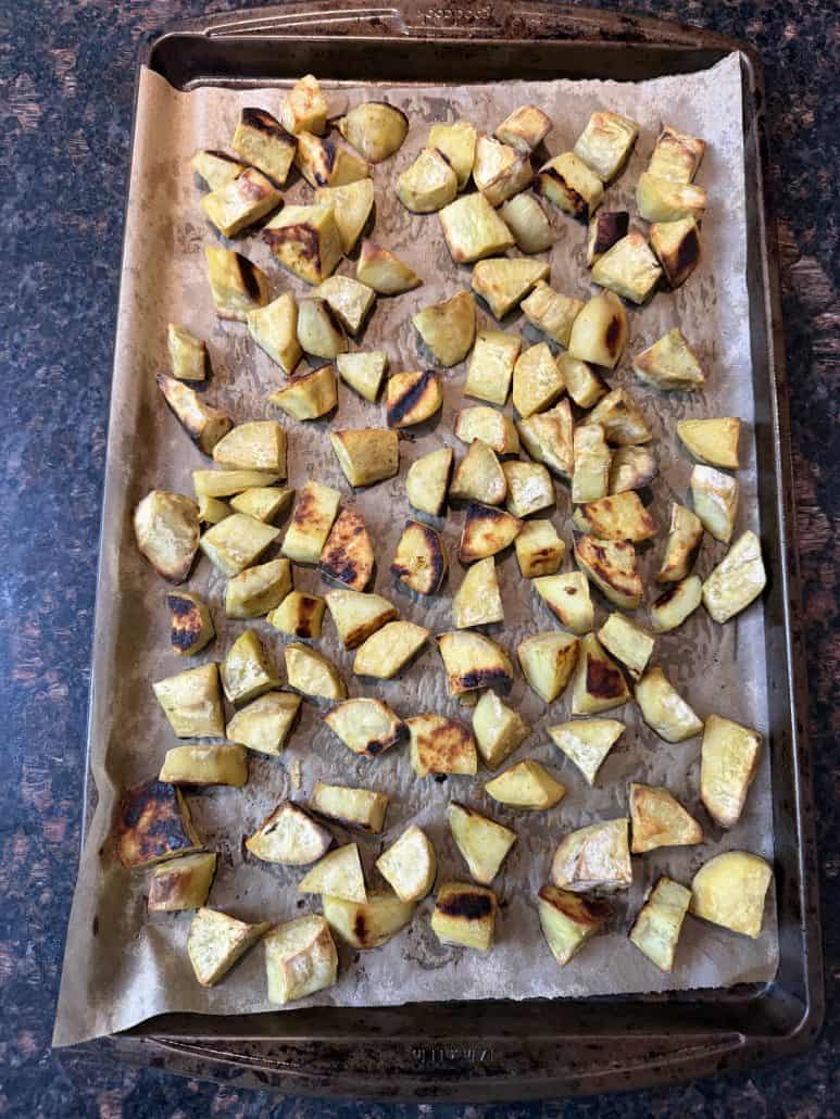 Roasted white sweet potato chunks spread out on a parchment-lined baking sheet, fresh out of the oven.