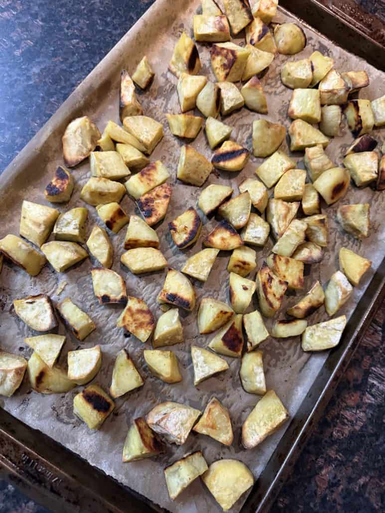 Golden brown roasted white sweet potatoes on a parchment-lined baking sheet, showing even browning and crispy edges.