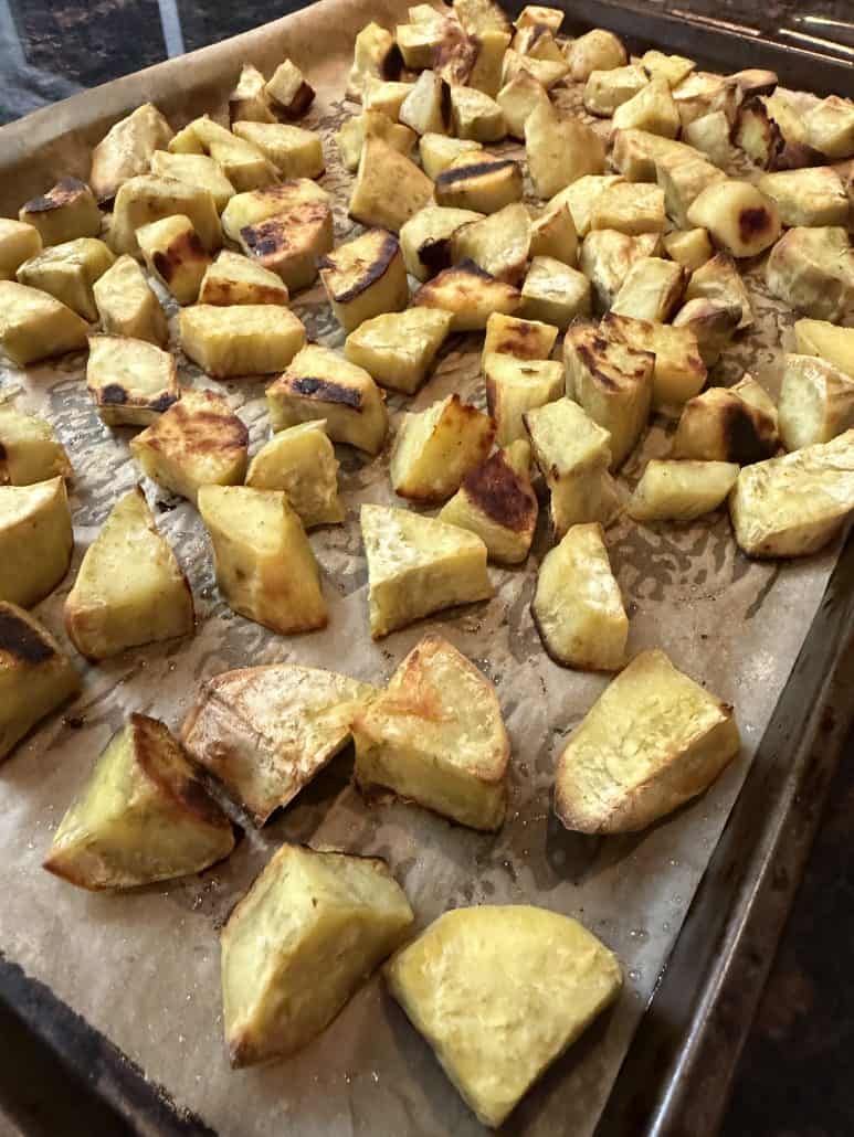 Close-up of roasted white sweet potato chunks on a baking sheet, highlighting their crispy edges and golden brown texture.