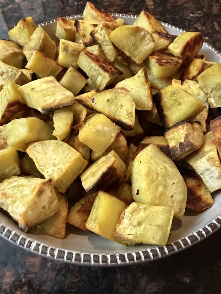 Close-up of a serving bowl filled with golden roasted white sweet potato chunks.