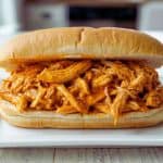 Pulled chicken sandwich on a soft roll, showcasing tender shredded chicken coated in flavorful sauce, perfect for a quick and satisfying meal.