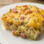 Cheesy ham and hash brown casserole served on a white plate, showing melted cheese and diced ham on top.