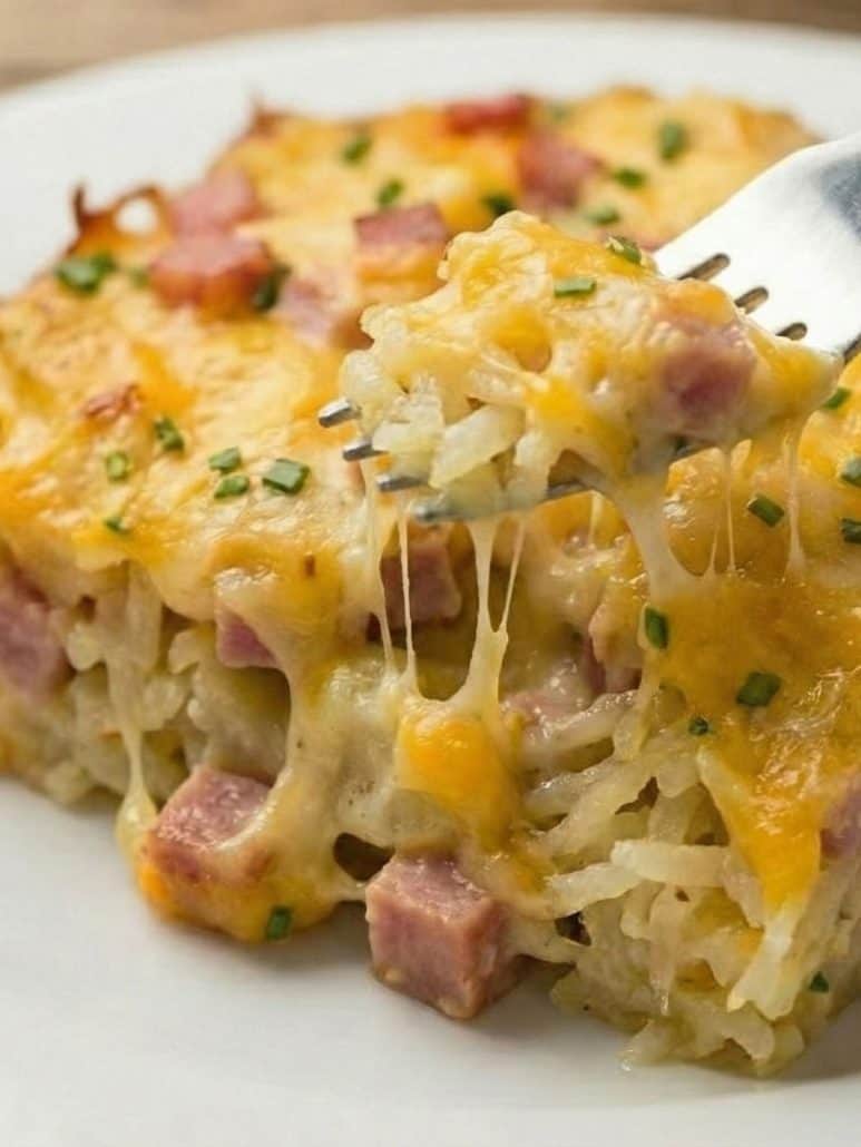 Close-up of cheesy ham and hash brown casserole with gooey melted cheese being pulled by a fork—perfect for a warm and comforting breakfast dish.