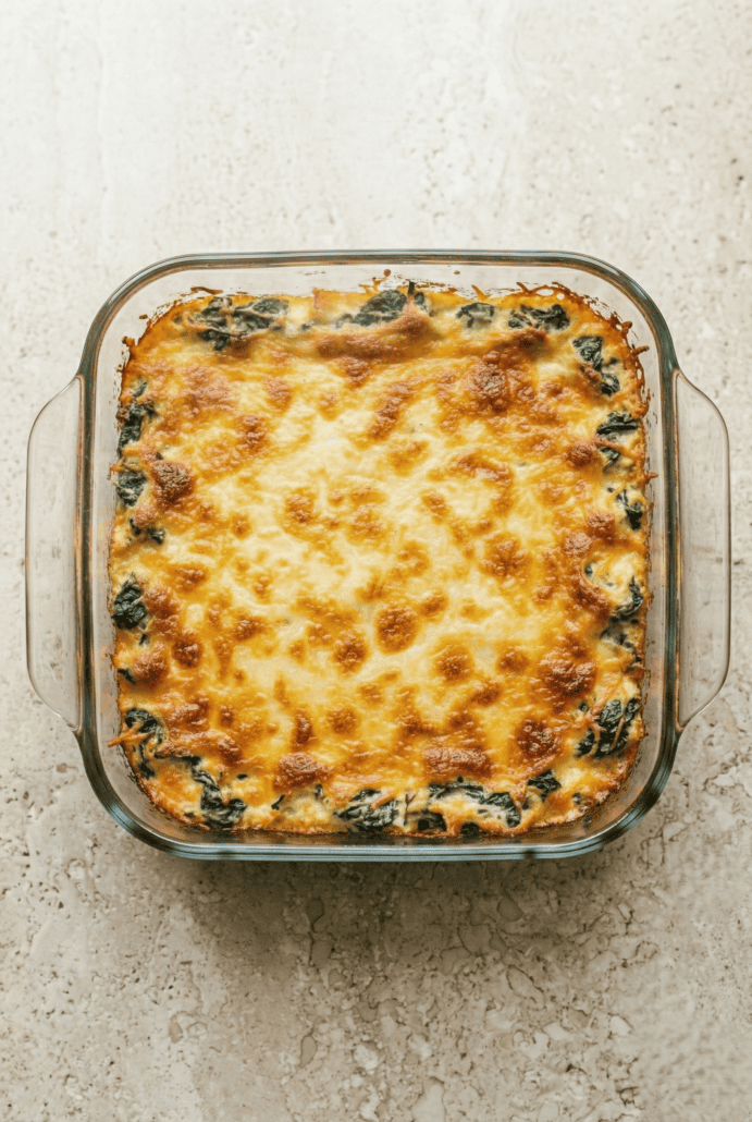 Freshly baked spinach artichoke dip in a glass dish with a golden brown cheesy top. Just out of the oven and ready to serve.