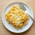 A serving of baked macaroni and cheese on a white plate with a fork, showing the golden, cheesy top from the oven.