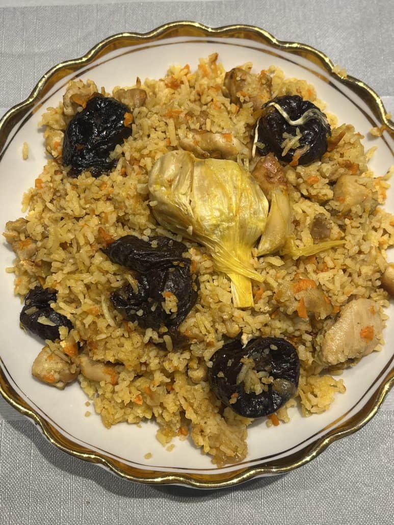 Plate of One-Pot Chicken and Rice Pilaf with prunes, garlic bulb, and tender chicken.