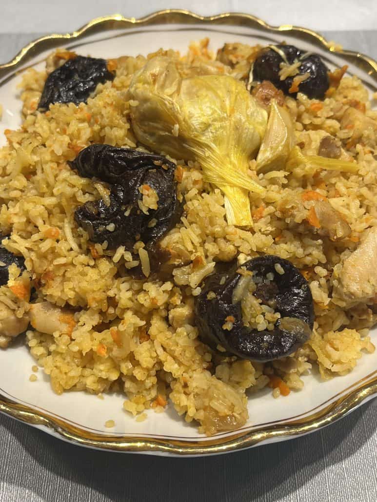 Close-up of One-Pot Chicken and Rice Pilaf showing fluffy rice, whole garlic bulb, tender chicken pieces, and sweet prunes.