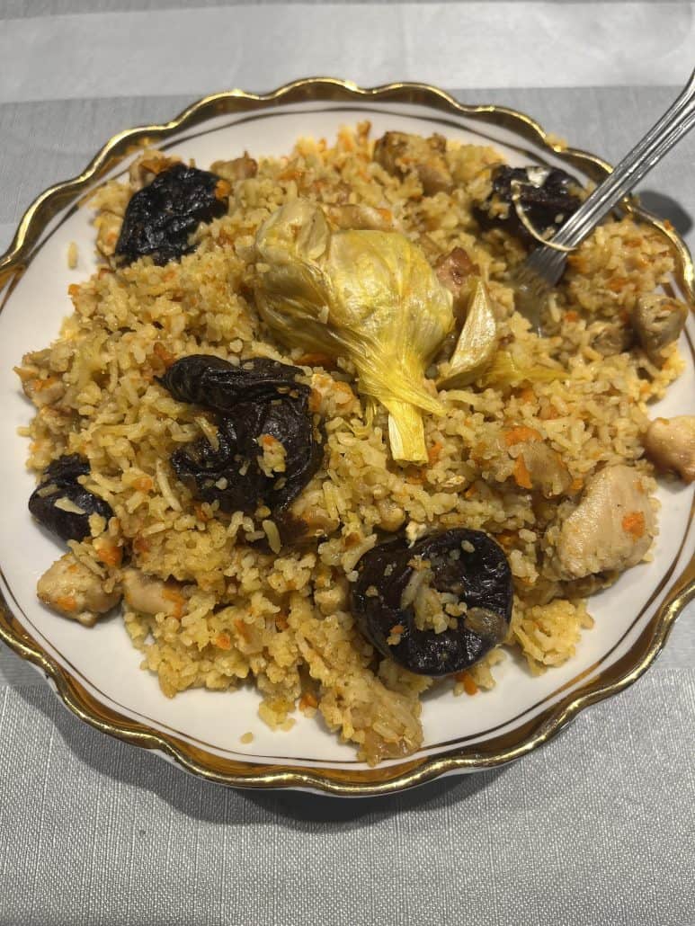 Homemade One-Pot Chicken and Rice Pilaf on a plate with a fork, highlighting tender chicken, whole garlic, and prunes.