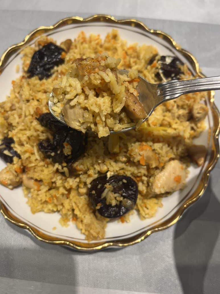 Forkful of One-Pot Chicken and Rice Pilaf lifted from the plate, showing tender chicken, rice, and prunes from the homemade stovetop recipe.