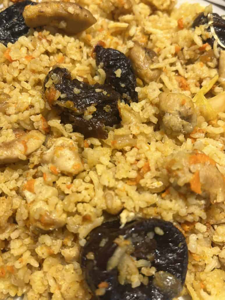 Close-up of stovetop Chicken and Rice Pilaf featuring soft rice, chunks of chicken, and sweet prunes, as prepared in the one-pot recipe.