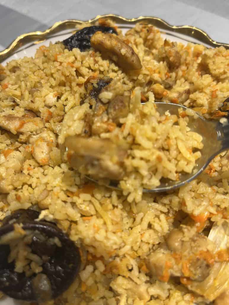 Close-up of a spoonful of One-Pot Chicken and Rice Pilaf showing fluffy rice, tender chicken, and prunes.