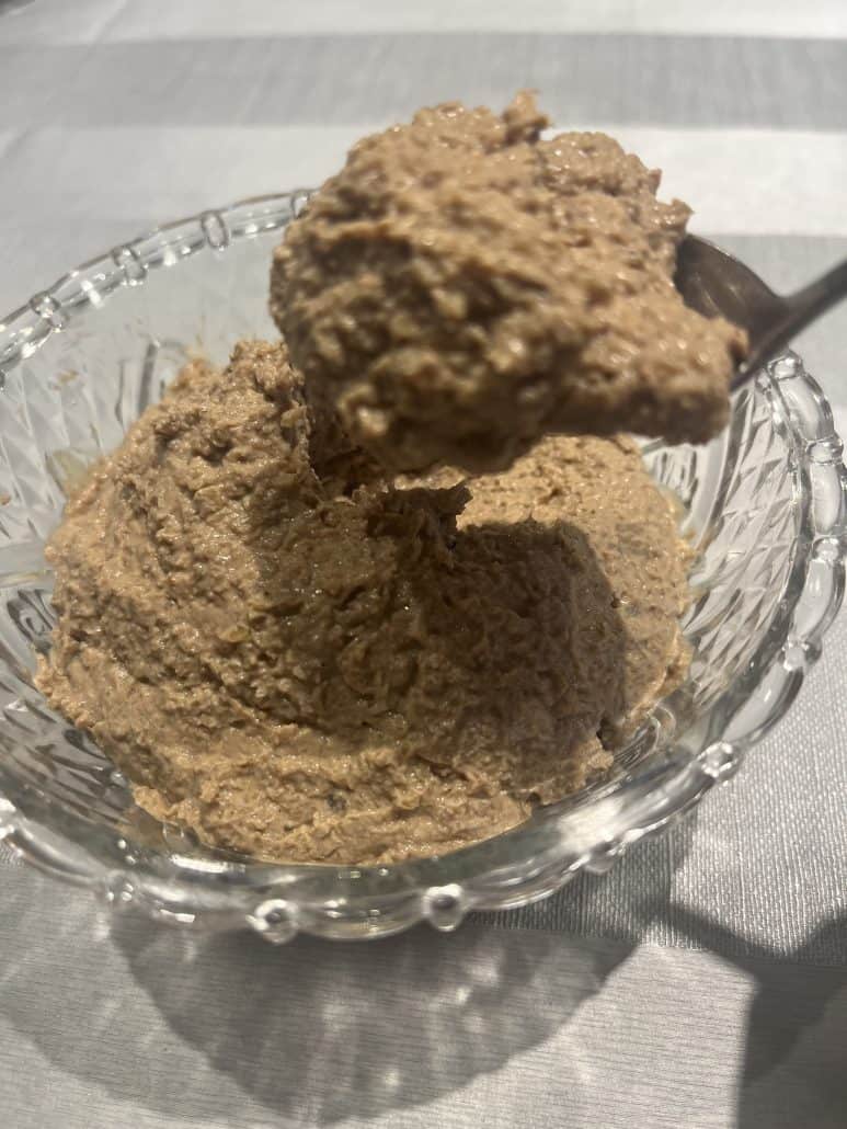 Spoonful of creamy chopped liver lifted from a glass bowl, showcasing the smooth texture.
