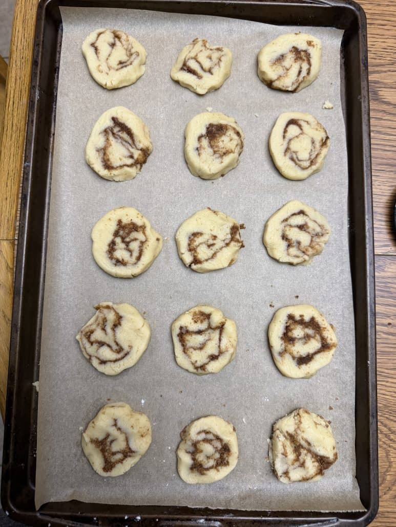 Unbaked cinnamon roll cookie slices arranged on a parchment-lined baking sheet, ready for the oven.