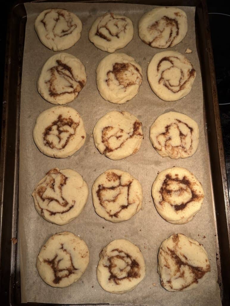 Freshly baked No Chill Cinnamon Roll Cookies on a parchment-lined baking sheet, just out of the oven.