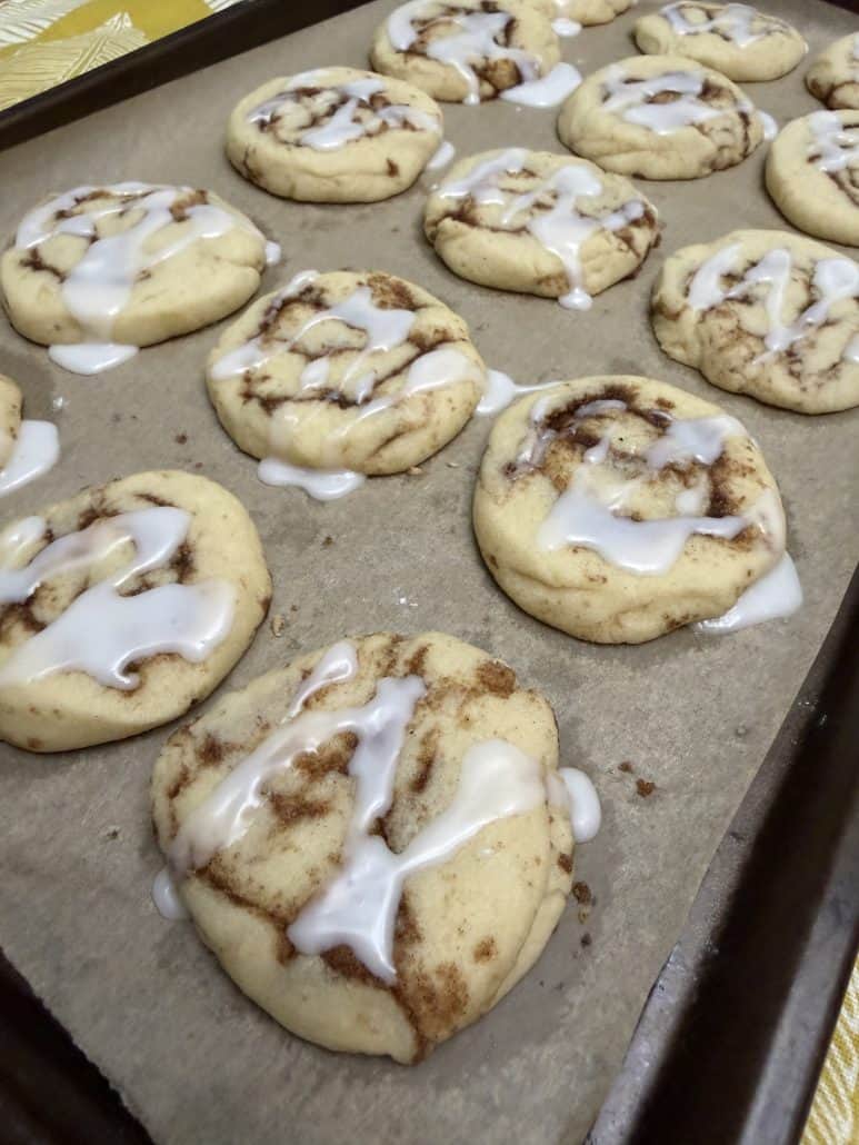 Side view of glazed No Chill Cinnamon Roll Cookies on a baking sheet, showing soft texture and cinnamon swirls.