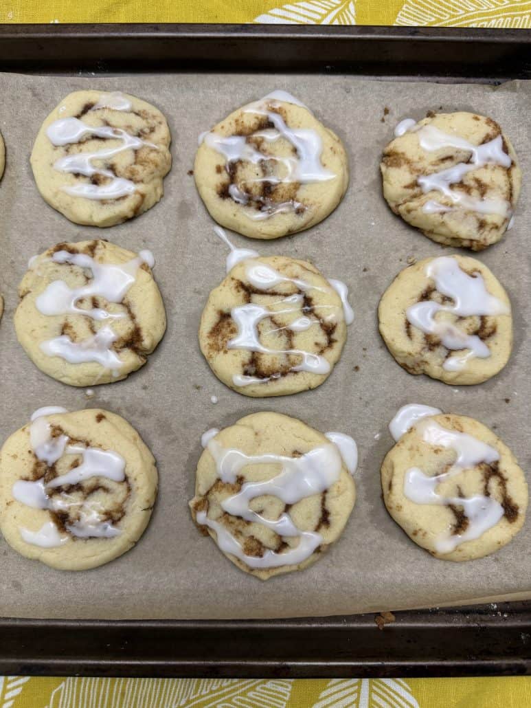 Top view of baked No Chill Cinnamon Roll Cookies with icing on parchment paper, arranged neatly in rows.