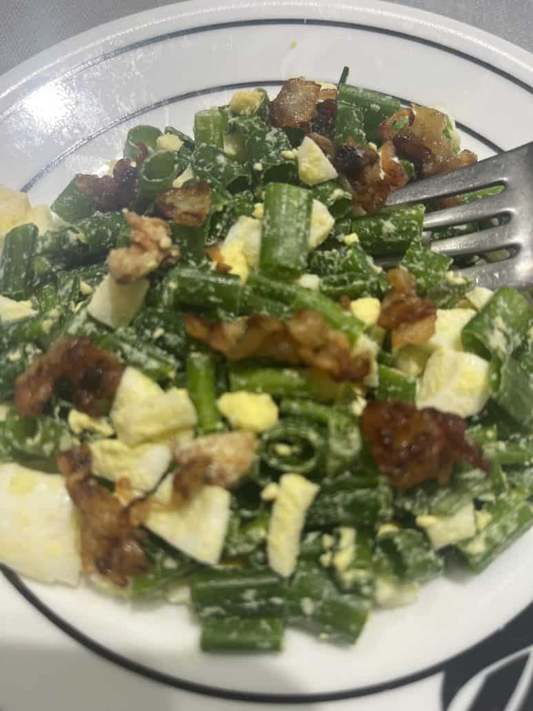 Fork resting on a plate of Green Onion, Egg, and Bacon Salad.