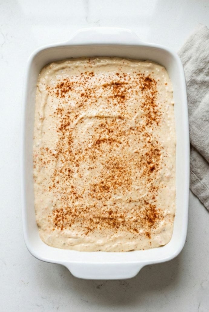 A baking dish filled with creamy crab dip, topped with a sprinkle of paprika before baking.