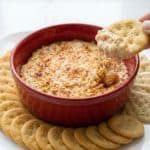Creamy hot crab dip served with crackers, with melted cheese stretching as a cracker is dipped into the dish.