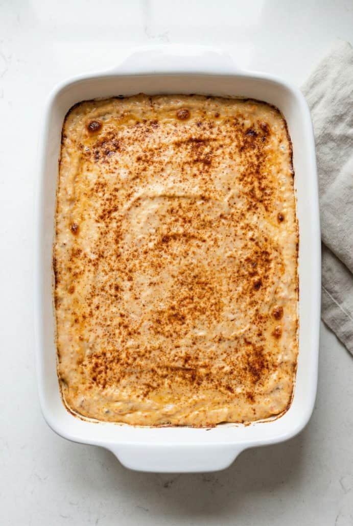 Baked hot crab dip in a white dish, golden and bubbling with a sprinkle of paprika on top, ready to be served as a warm, creamy appetizer.