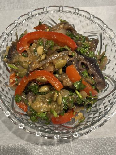 Glass bowl filled with marinated eggplant and bell pepper salad, showing colorful strips of red pepper, cooked eggplant, parsley, and pumpkin seeds.