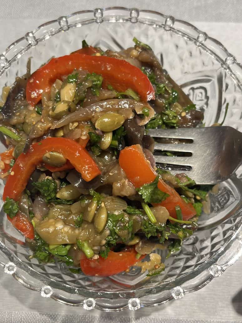 Overhead view of marinated eggplant and bell pepper salad with a fork in a glass bowl, showcasing the fresh, colorful ingredients.