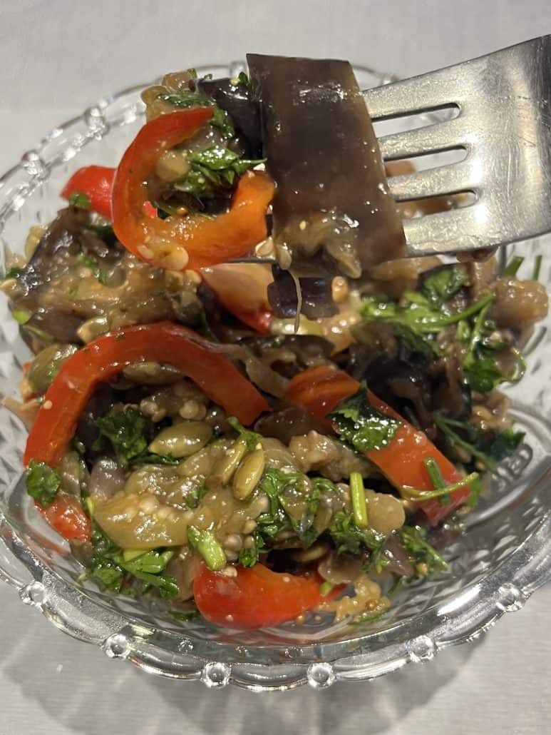 Fork lifting a bite of marinated eggplant and bell pepper salad from a glass bowl, highlighting the vibrant textures and flavors.