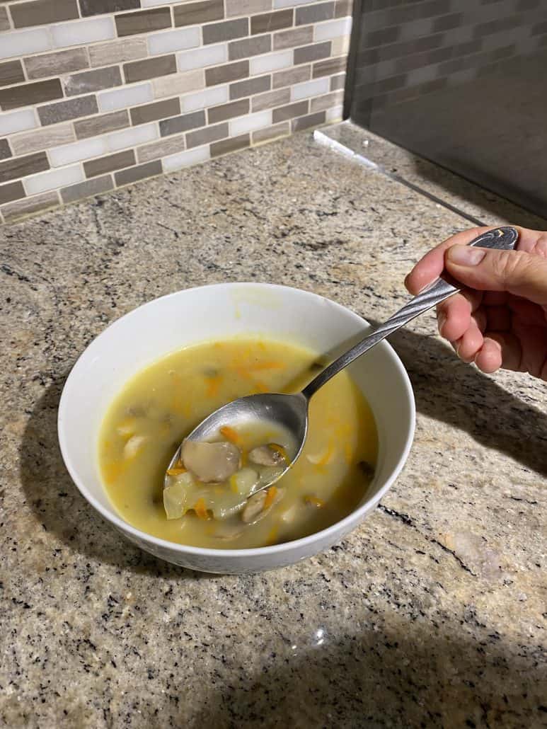 Close-up of a spoonful of chunky mushroom soup being lifted from a bowl, showing the tender potatoes, mushrooms, and carrots featured in the recipe.