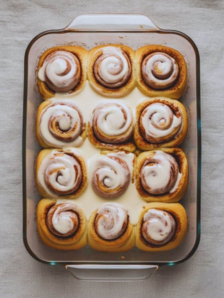 A full batch of overnight cinnamon rolls baked in a glass dish, topped with vanilla glaze.