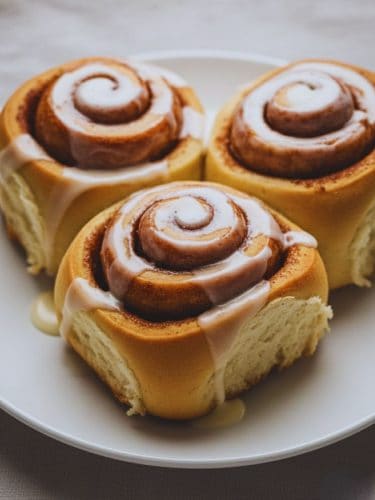 Easy Overnight Cinnamon Roll Recipe From Scratch Freshly baked overnight cinnamon rolls topped with vanilla glaze, served warm on a white plate.