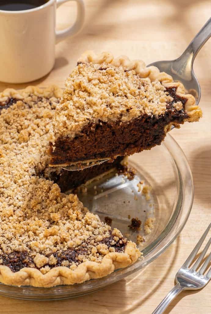 Slice of Shoofly Pie being lifted from a glass pie dish, showing the rich molasses filling and crumb topping.
