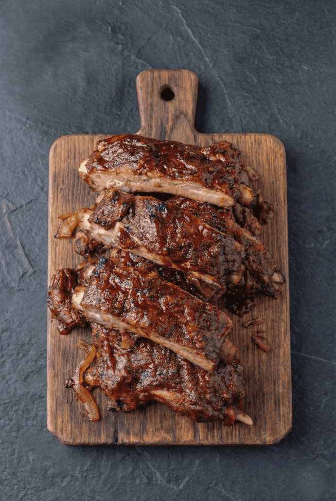 Tender slow cooker baby back ribs with BBQ sauce served on a wooden cutting board.