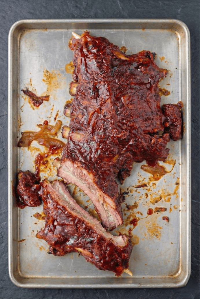 Oven-finished slow cooker baby back ribs sliced on a baking sheet, showing juicy, tender meat and caramelized BBQ glaze.
