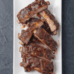Slow cooker baby back ribs glazed with BBQ sauce on a white platter. Tender, juicy, and caramelized from the oven finish.