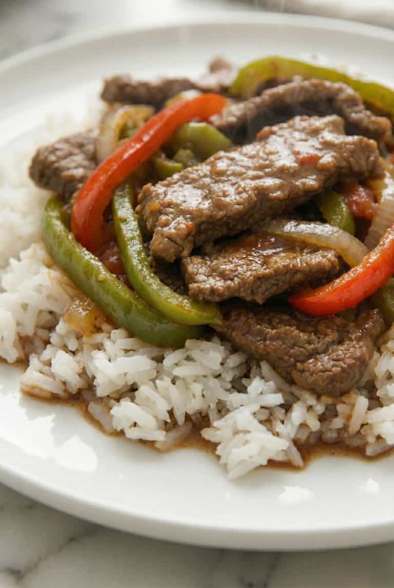 Slow Cooker Pepper Steak served over white rice with bell peppers and onions.