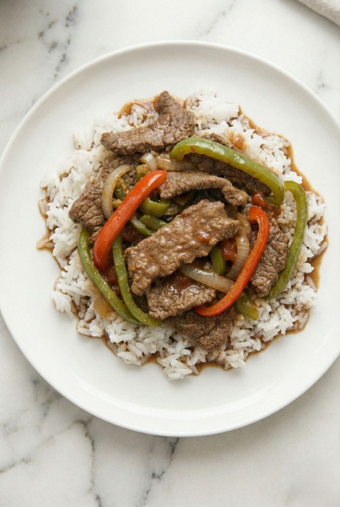 Slow Cooker Pepper Steak served over fluffy white rice on a white plate.