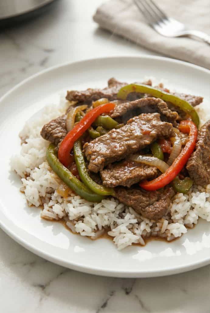 Plate of Slow Cooker Pepper Steak with bell peppers and onions served over rice. A cozy and flavorful meal from this easy crockpot recipe.