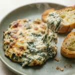 Hot spinach artichoke dip served on a plate with toasted bread, showing a cheesy pull perfectly, capturing the creamy, baked appetizer recipe.