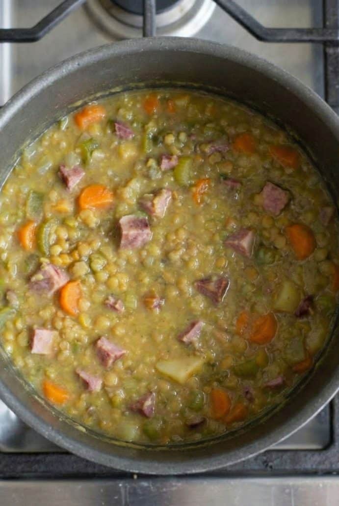 Close-up view of split pea soup with chunks of ham, carrots, and celery simmering in a pot.