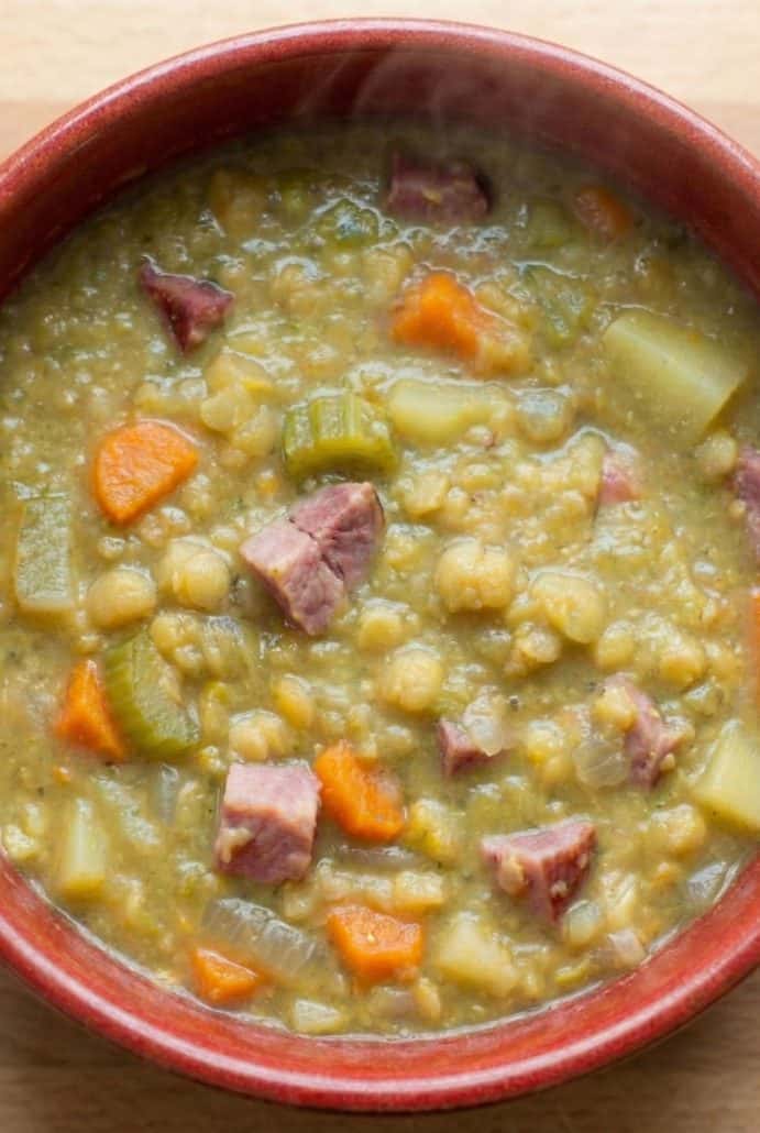 Steaming bowl of thick split pea soup with ham, carrots, and celery, highlighting the hearty finished dish.