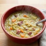 A steaming bowl of homemade split pea soup with ham, carrots, and celery, as featured in the comforting stovetop recipe.
