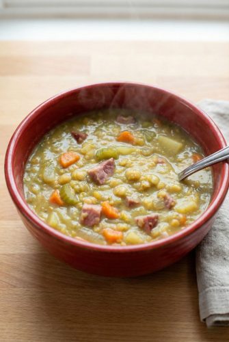 A steaming bowl of homemade split pea soup with ham, carrots, and celery, as featured in the comforting stovetop recipe.