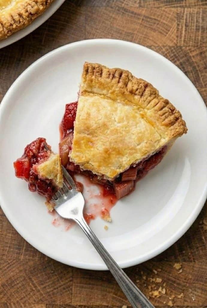 Partially eaten slice of strawberry rhubarb pie on a white plate with a fork, showing the juicy filling and flaky crust.