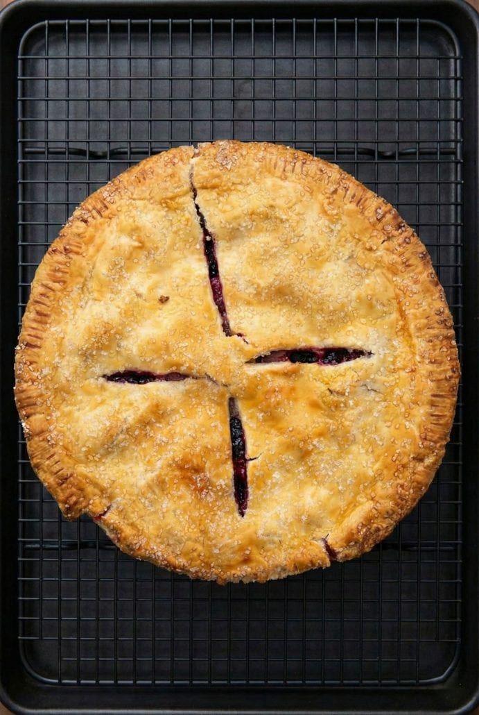 Whole baked strawberry rhubarb pie with a golden crust and steam vents, cooling on a wire rack as shown in the step-by-step instructions.